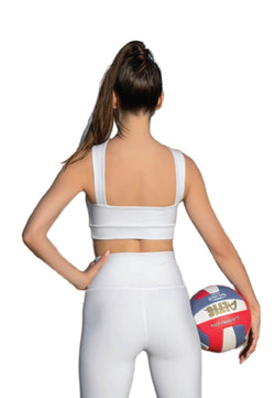 Frau, die Lisminas 190 Decoltée Sport-BH in Weiss trägt, hält einen Volleyball und blickt weg.