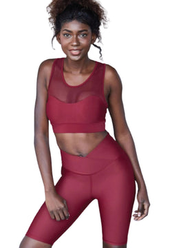 Person in Lismina Bordeaux-Biker-Leggings und Netzoberteil, lächelt vor weißem Hintergrund.