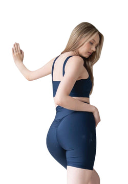 Eine Frau in Lisminas marineblauer 8007 Scrunch Butt Short posiert mit einem Arm an einer Wand und blickt zur Seite.