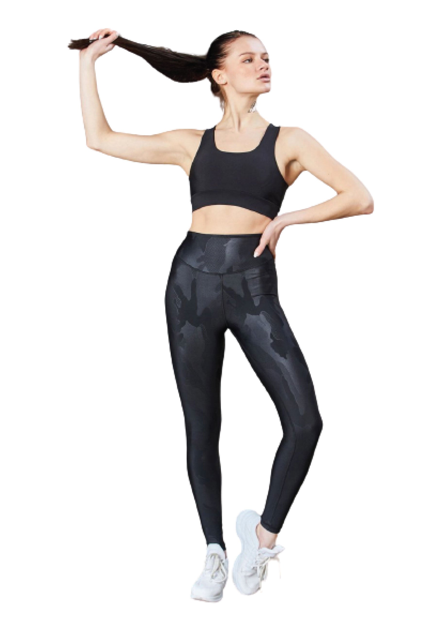 Person in Sportkleidung, die einen Pferdeschwanz zieht und Lisminas schwarze 1058-Leggings in Lederoptik, einen Sport-BH und weiße Turnschuhe trägt.