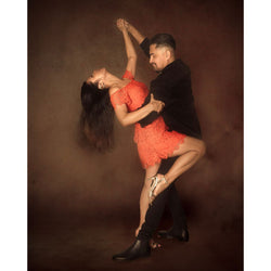 Ein Paar tanzt Salsa: Sie trägt ein orangefarbenes Kleid, er ein schwarzes. Beide sind Teil des Flyingdance-Erlebnisses der Tanzkurse.