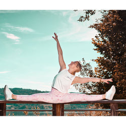Eine Person genießt die Tanzkurse „Online Dance, Fitness & Yoga“ von Sandra Burdet, während sie auf einem Holzgeländer einen Spagat macht.