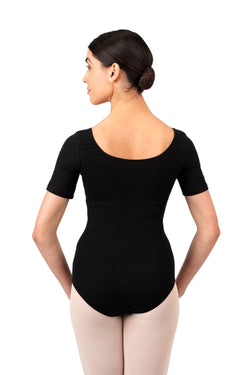 Person in Rumpfs schwarzem Kurzarm-Body-Leotard, beiger Strumpfhose, Duttfrisur, blickt über die Schulter.