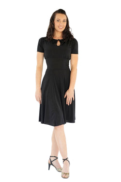 Frau im Rumpf RU5751 Augusta Kurzarm-Kleid und High Heels lächelnd vor weißem Hintergrund.