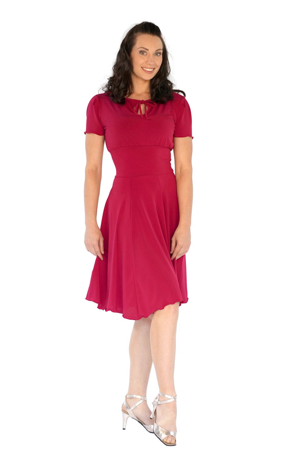 Eine Person in einem RU5751 Augusta Kurzarm-Kleid von Rumpf und silbernen Absätzen, lächelnd vor weißem Hintergrund.