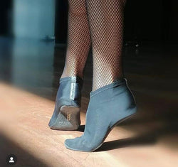 Person in Netzstrumpfhose und PD ComfyProtect Tanzschuhen von Portdance, die auf Zehenspitzen auf einem sonnenbeschienenen Holzboden steht.