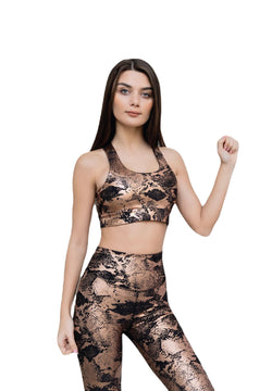Eine Frau posiert selbstbewusst in einem Lismina 235 Gold & Schwarz Crossed Sports Bra mit Schlangenhautmuster und präsentiert den Rücken.