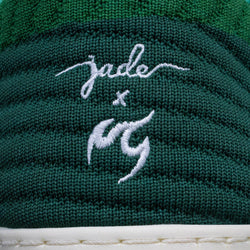 Nahaufnahme des grünen Stoffes der Fuego-Tanzschuhe mit den weiß aufgestickten Initialen „Jade“ und Tanzsneaker darunter.